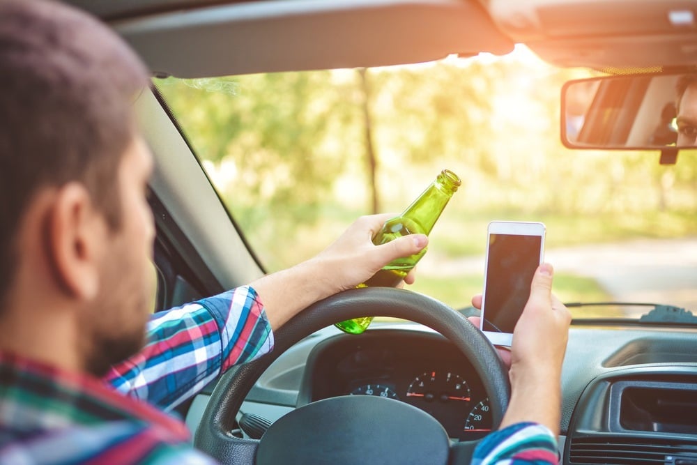 Guy holding a beer bottle and checking his phone behind the wheel